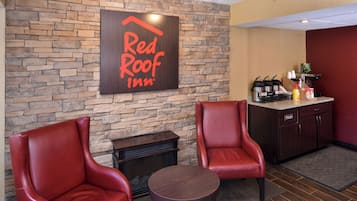 A Red Roof Inn lobby with stone walls, leather armchairs, a small round table, and a coffee station.