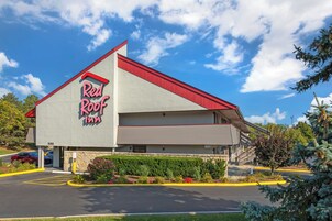 Un Red Roof Inn con tejado rojo, fachada de piedra y estacionamiento con bordes amarillos.