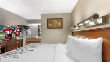 Una habitación de hotel con cama, televisión, espejo y un cuadro en la pared.