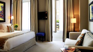 Une chambre d’hôtel avec un lit, un canapé, une télévision et une fenêtre avec des rideaux.