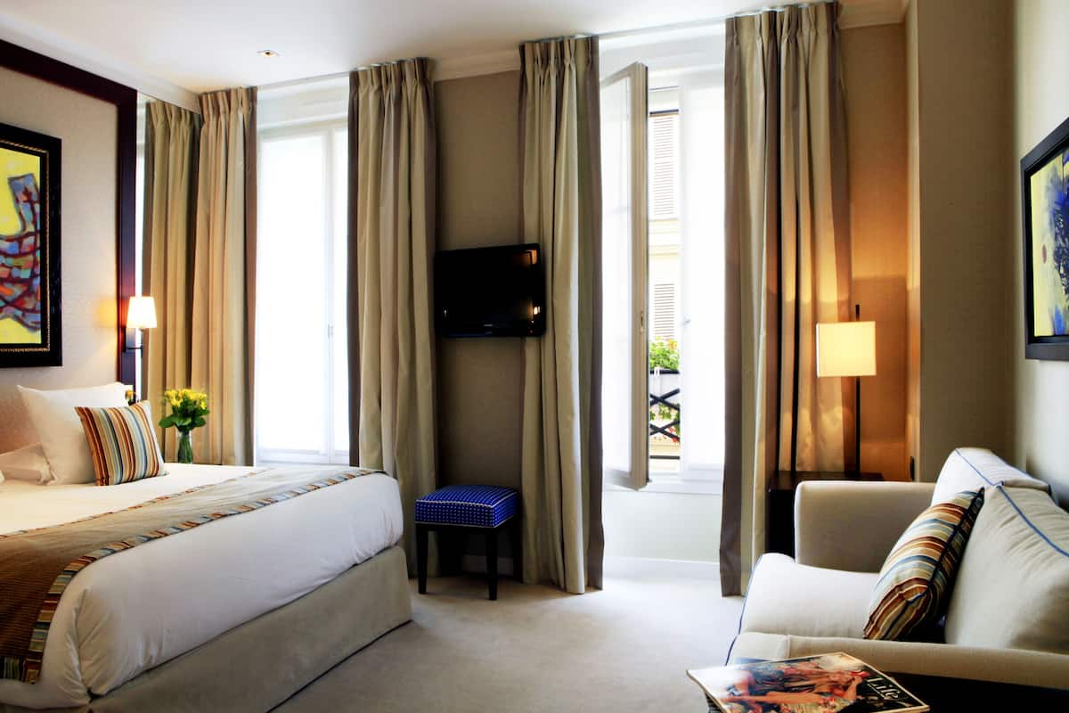 A hotel room with a bed, a sofa, a television, and a window with curtains.