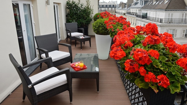 Un balcon agrémenté de meubles en osier, d’une table en verre et d’une plante en pot aux fleurs rouges.