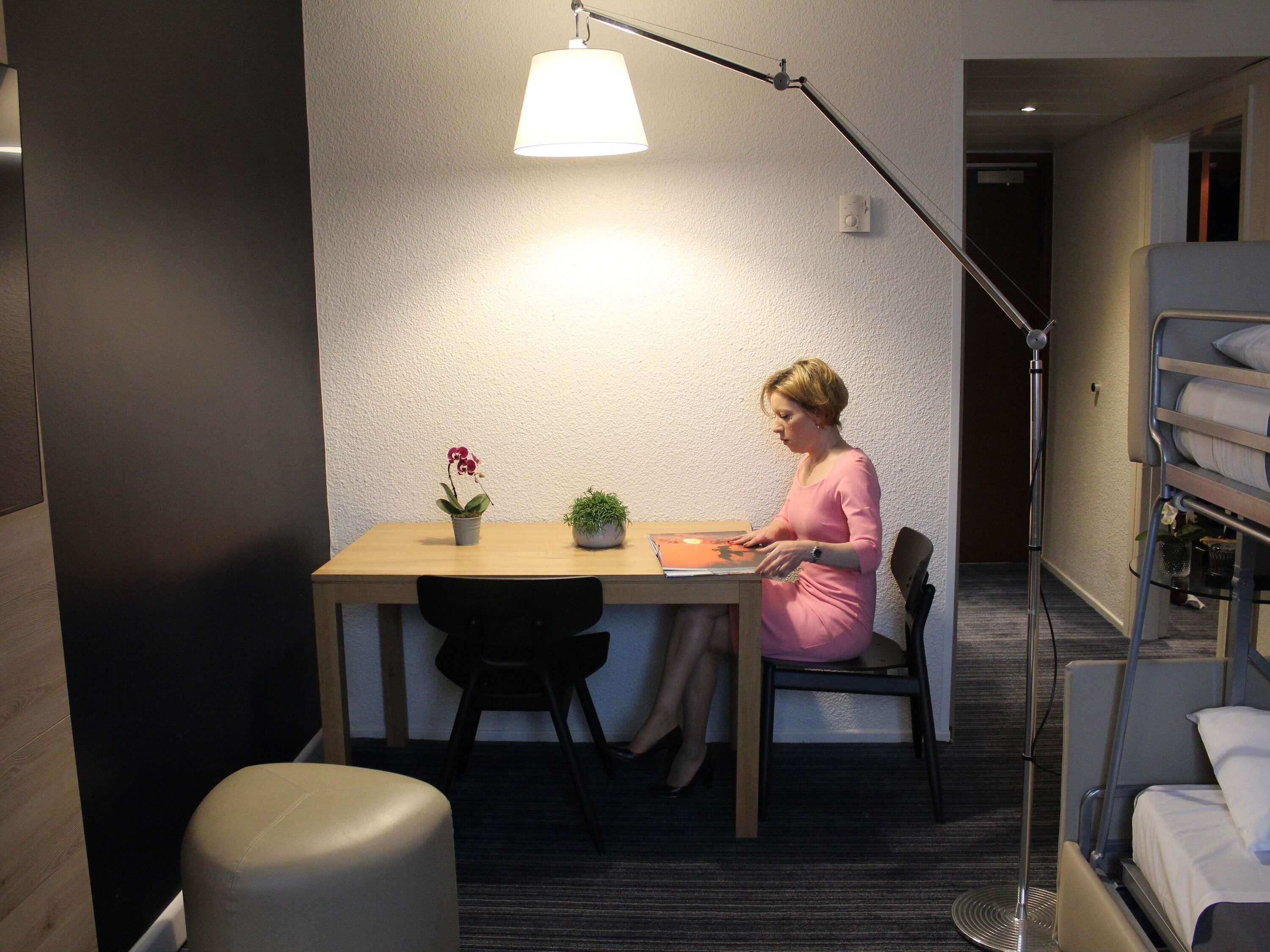 A small, modern room with a wooden desk, a chair, a lamp, and a bunk bed with white bedding.