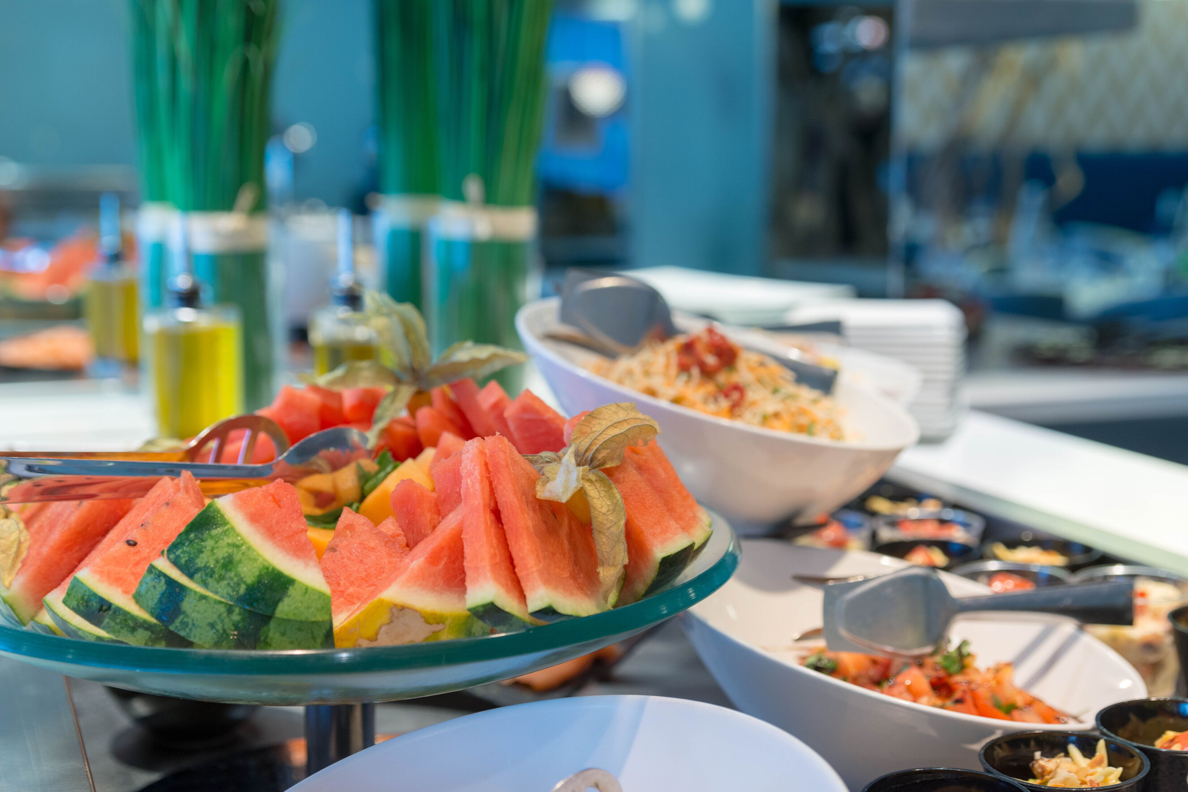 Buffet com diversos pratos, incluindo uma melancia como peça central e vários utensílios para servir.