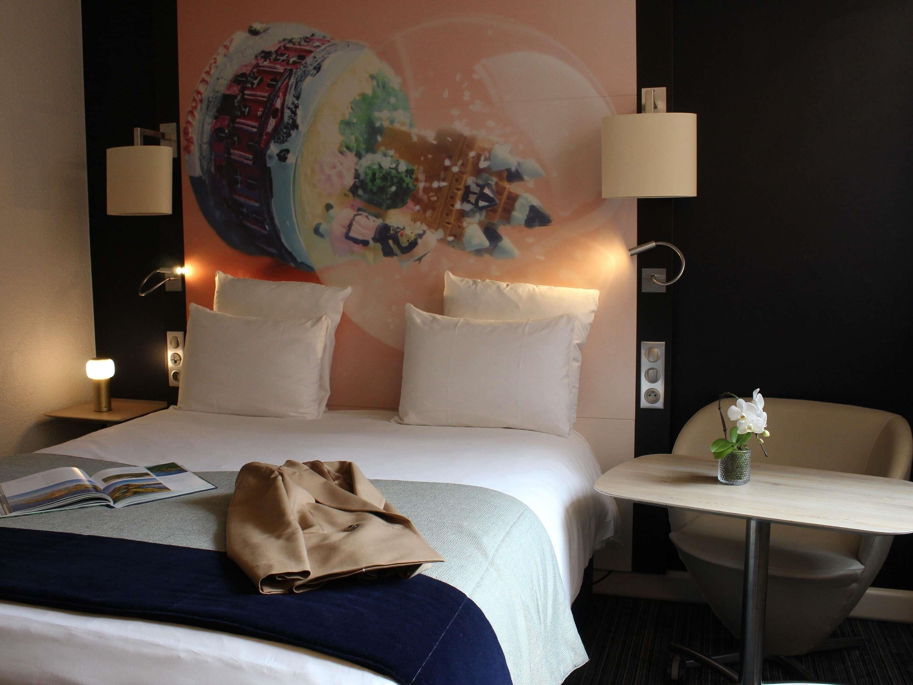 Une chambre d’hôtel comprenant un lit, une table de chevet, une chaise et une fresque murale.