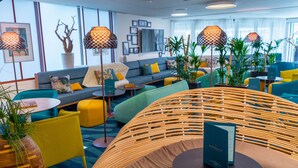 A modern hotel lobby with a sofa, chairs, and a wicker chair. There are potted plants and a table with a menu. - Mercure Toulouse Centre Saint-Georges Hotel (Toulouse)