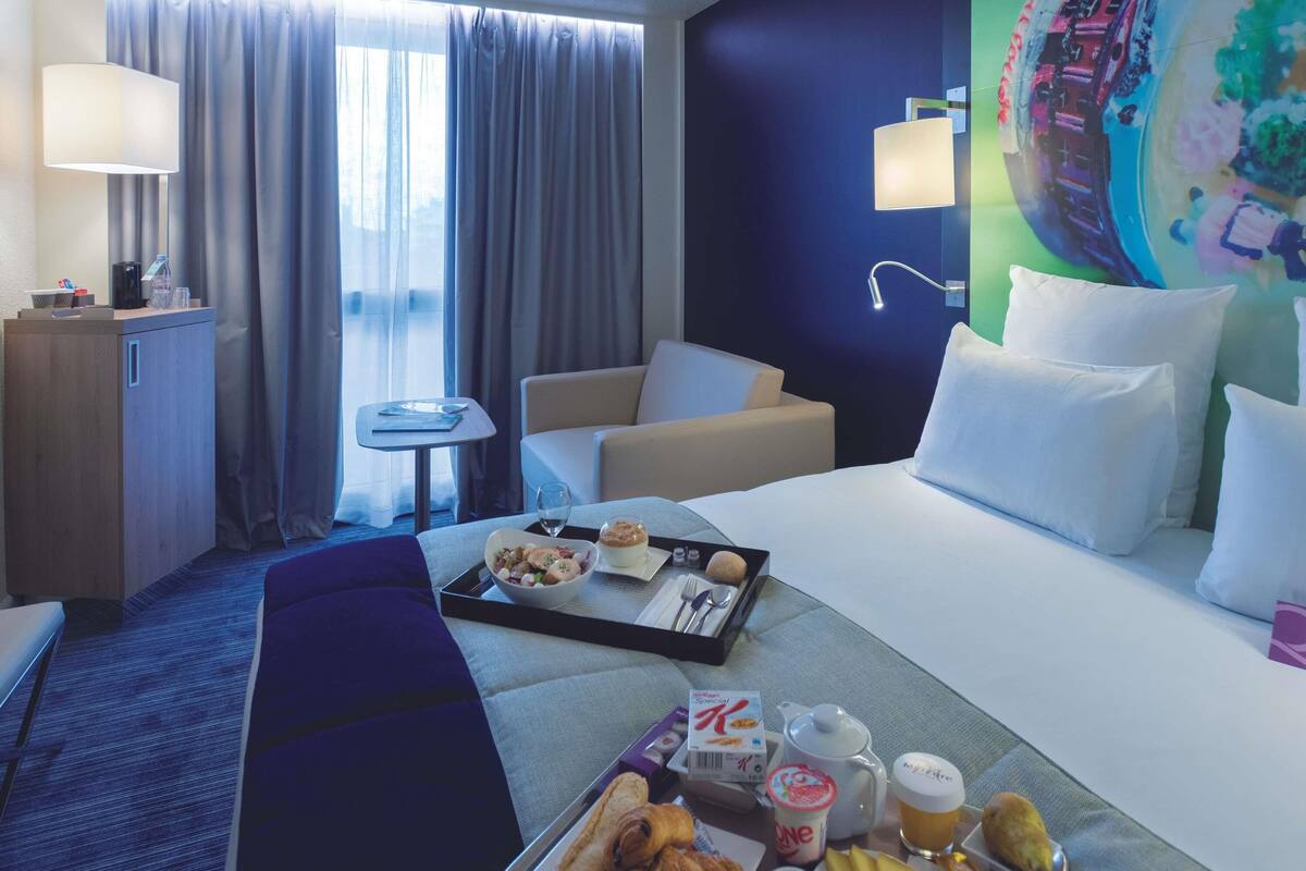 Ein Hotelzimmer mit Bett, Schreibtisch, Stuhl, kleinem Tisch und einem Fenster mit Vorhängen.