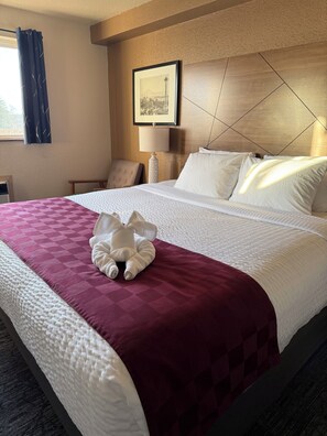 Una habitació d'hotel amb un llit ben fet, un quadre al mur, una làmpada i una cadira.