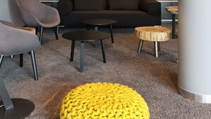 Una sala de estar moderna con un sofá oscuro, dos mesas de centro redondas, un taburete amarillo y una lámpara de pie.