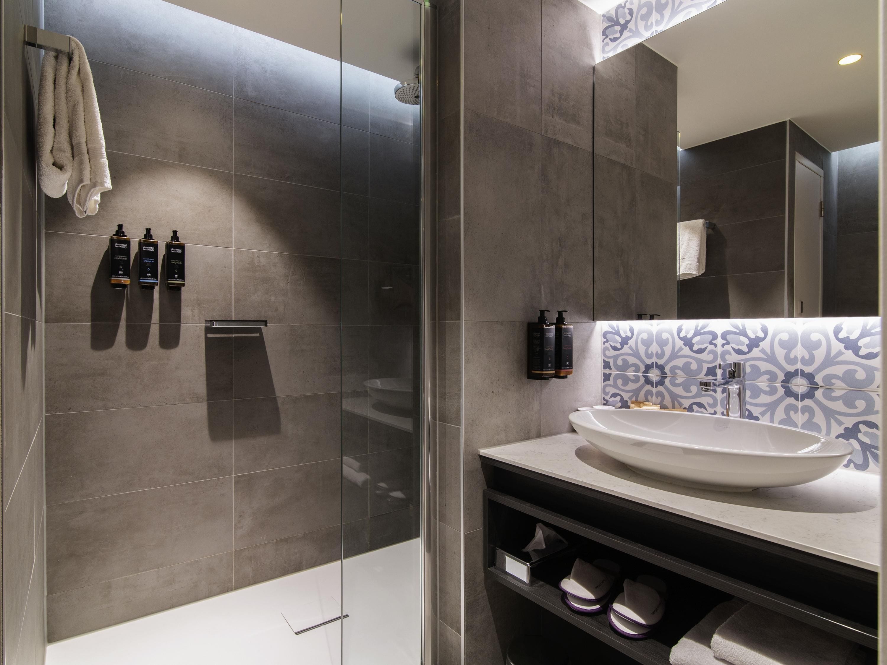 A modern bathroom with a glass shower enclosure, a white sink, and a vanity with a patterned backsplash.