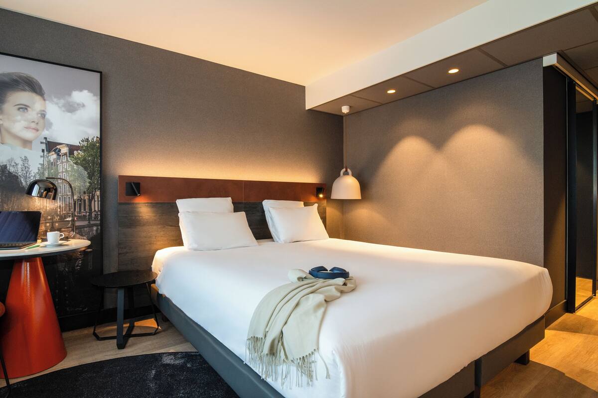 Habitación de hotel moderna con una cama grande, un escritorio con una computadora portátil y un cuadro enmarcado en la pared.