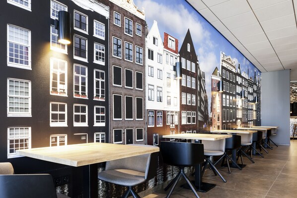 A restaurant with a mural of Amsterdam buildings, tables, and chairs. - Mercure Amsterdam City (Amsterdam)