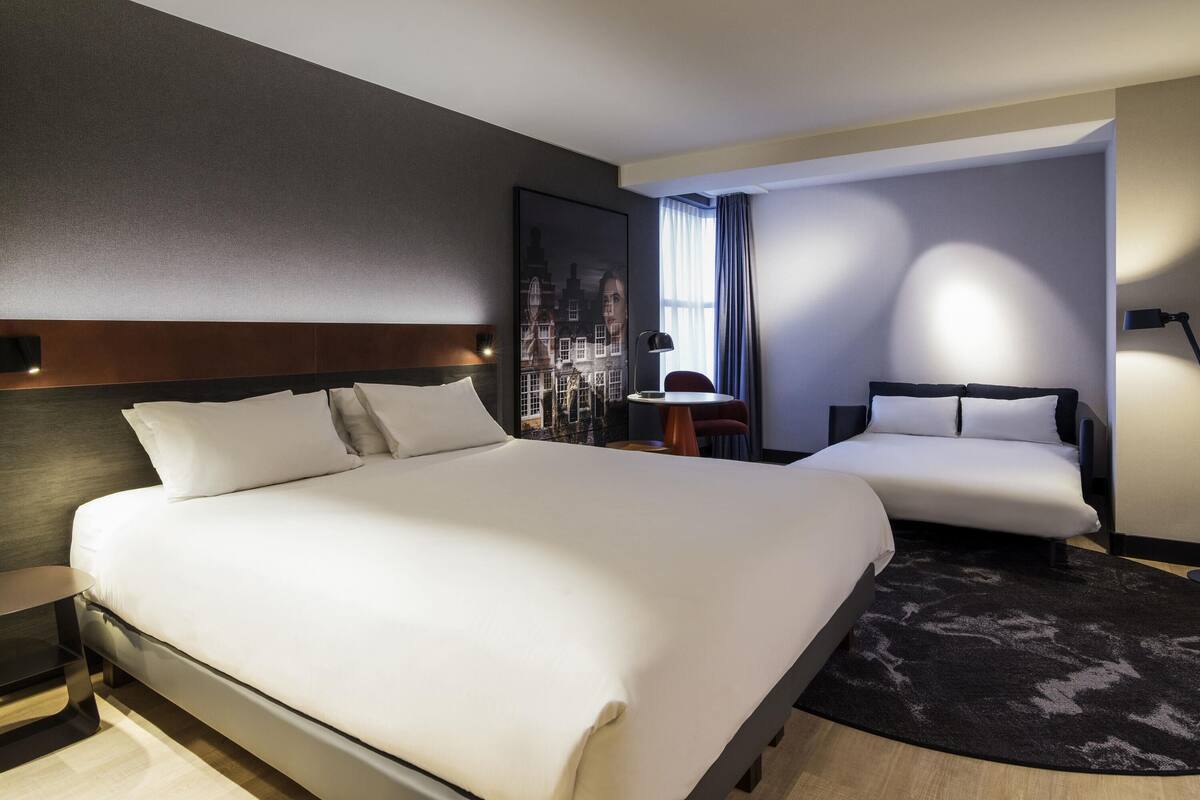 Habitación de hotel con una cama grande, una cama más pequeña, un escritorio y una silla.