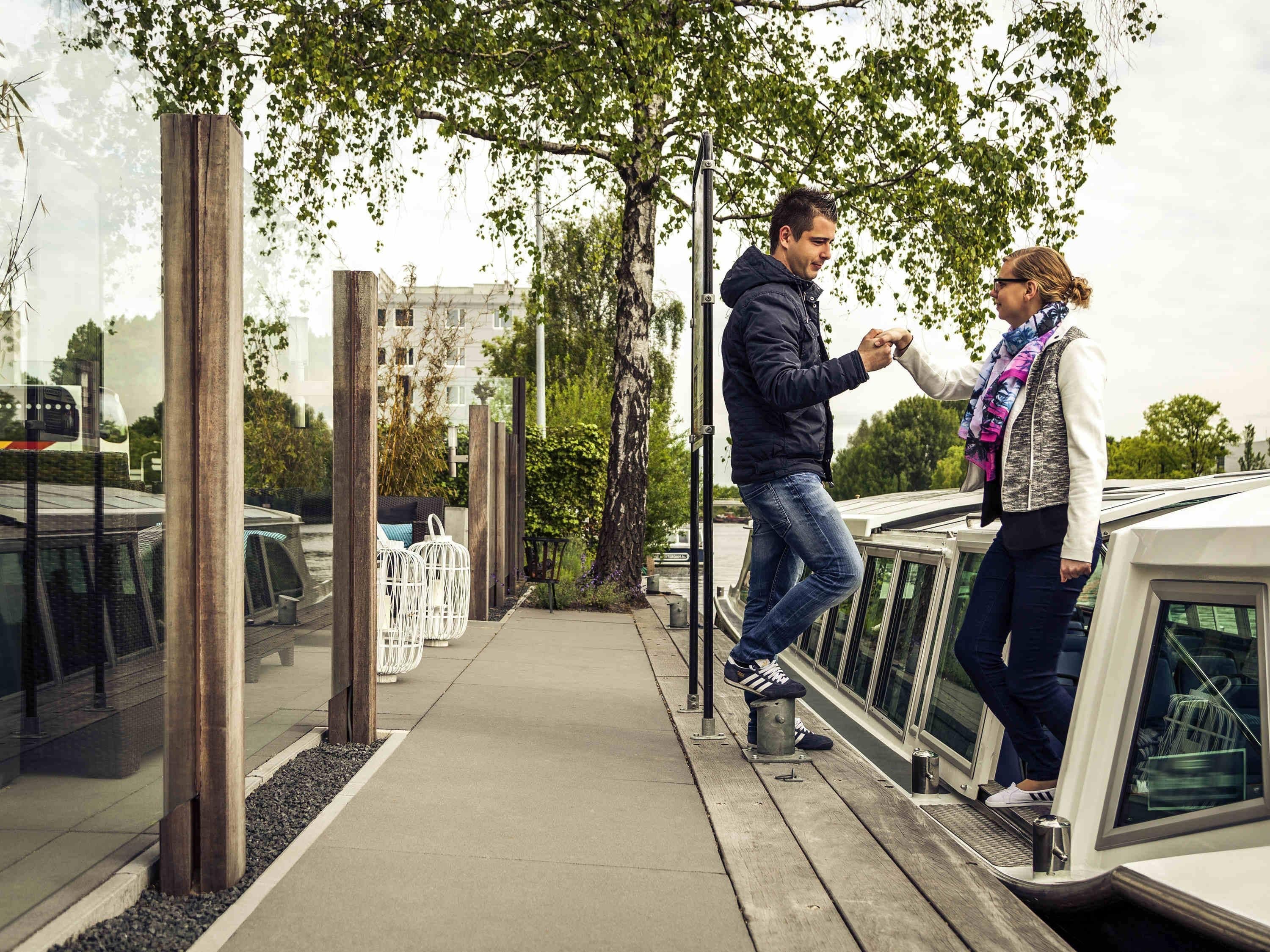 A man and a woman standing by a white vehicle, holding hands, with a sidewalk and greenery in the background.