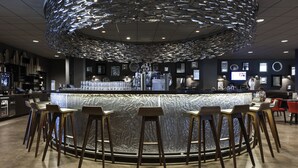 A bar area with a circular bar counter, wooden stools, and a unique ceiling light fixture.