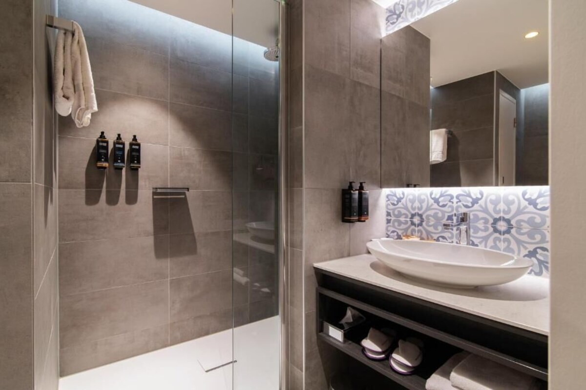 Un baño moderno con cabina de ducha de vidrio, un lavamanos grande con lavabo a la vista y un mueble de tocador con salpicadero decorativo.