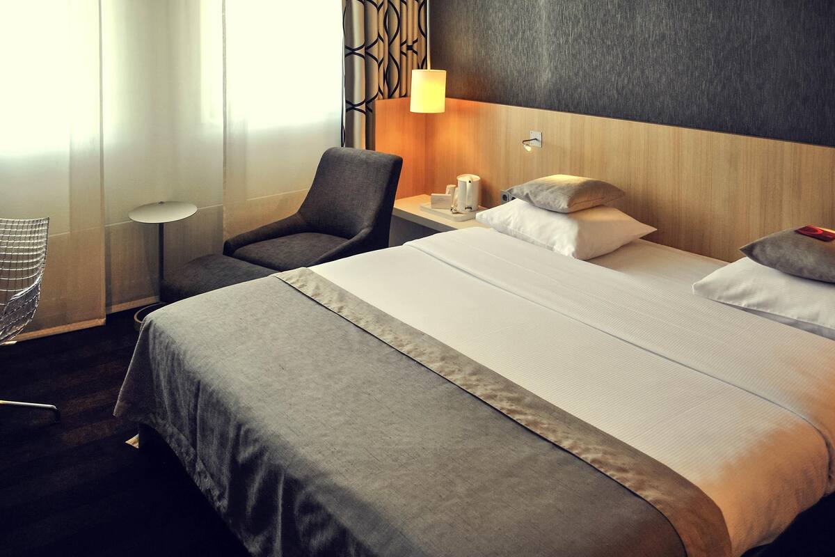 Habitación de hotel con cama, una silla, una mesita de noche con lámpara y pared con diseño geométrico.