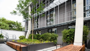 A modern building with a courtyard featuring a wooden bench, planters with greenery, and a staircase leading to an upper level. - Mercure München City Schwabing (Munich)