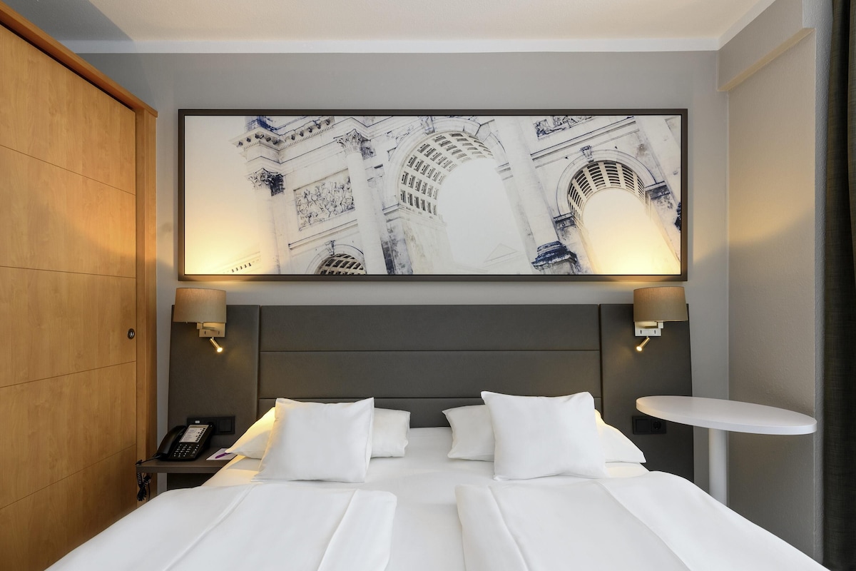 A hotel room with a large bed, two bedside tables, a phone, and a wall-mounted artwork.