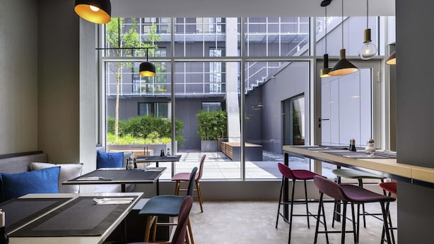 A modern restaurant with a view of a building and greenery outside. - Mercure München City Schwabing (Munich)