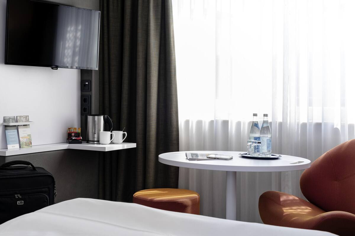 Een hotelkamer met een bed, een koffiezetapparaat, een kleintje tafeltje met waterflesjes, een televisie en een koffer.