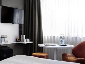 Habitación de hotel con cama, cafetera, una mesita con botellas de agua, televisión y maleta.