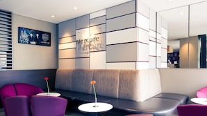 A modern hotel lobby with a seating area featuring purple chairs and a grey sofa. A sign reads "Mercure Hotels." - Mercure München City Schwabing (Munich)