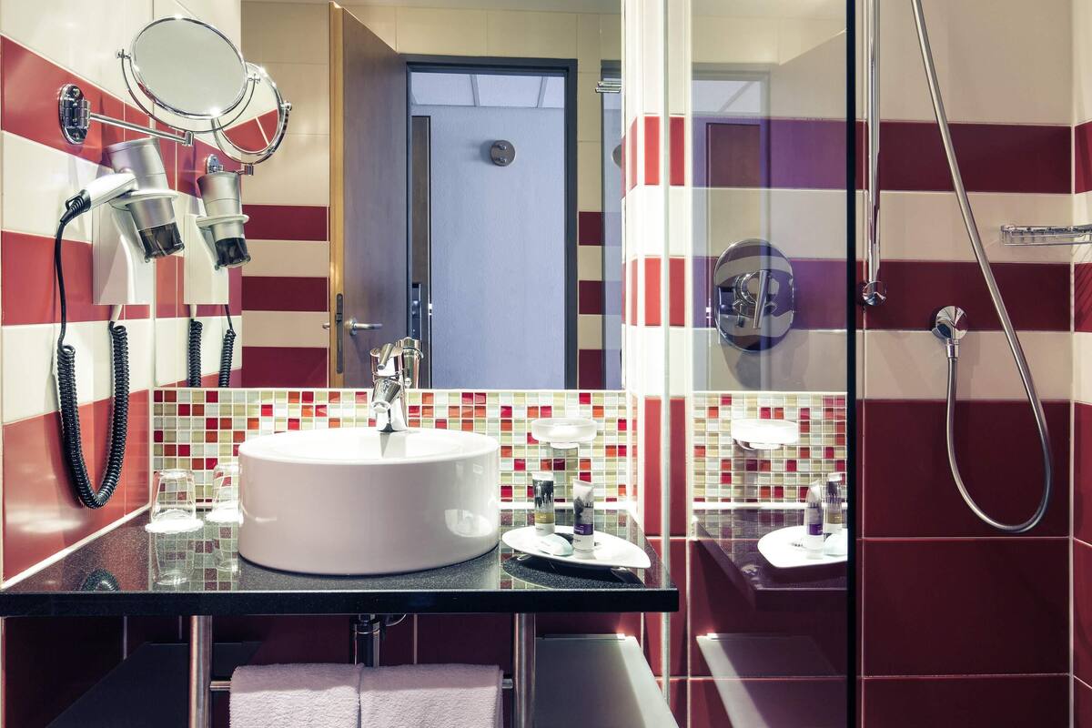 A modern bathroom with a large mirror, a round sink, and a shower.