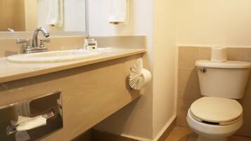 A bathroom with a sink, mirror, toilet, and towel dispenser.