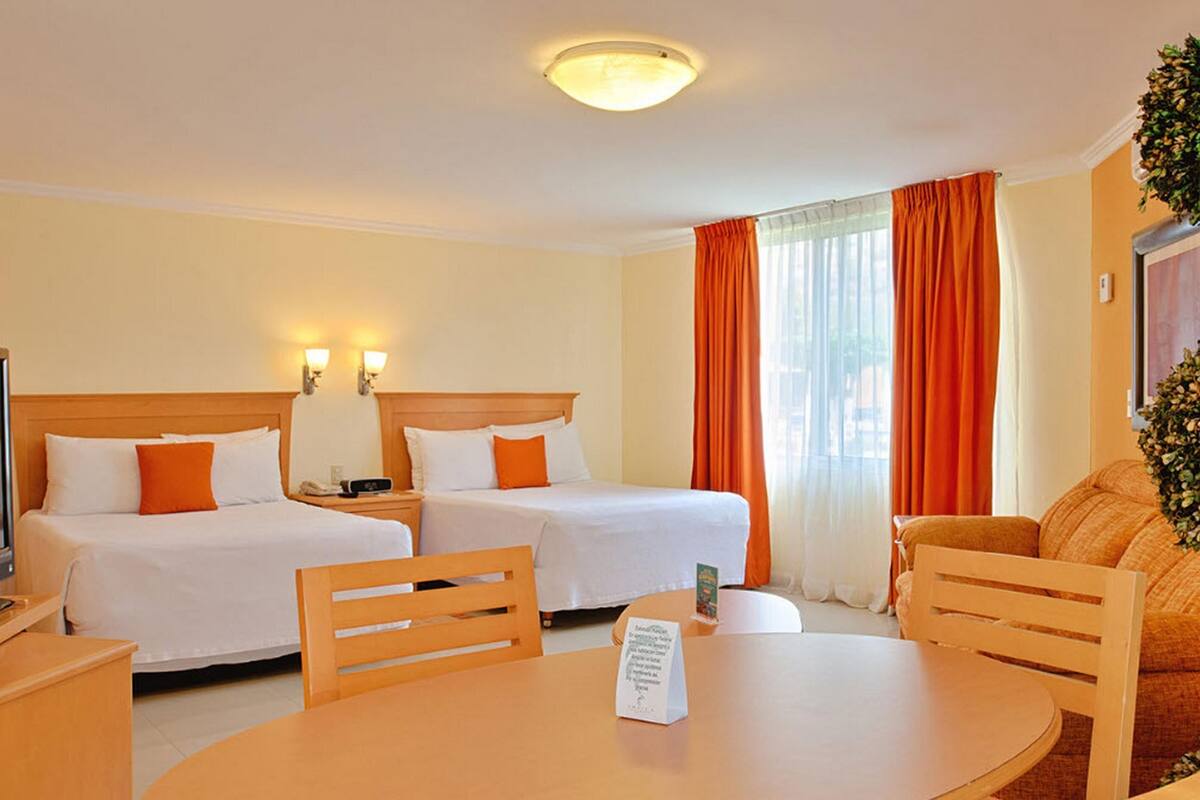 Een hotelkamer met twee bedden, een televisie, een tafel met stoelen en een plant.