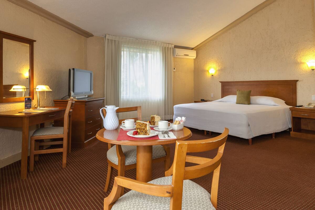 Een hotelkamer met een bed, een bureau met een televisie, een eettafel met een taart, en een stoel.