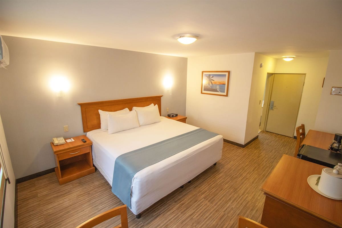 Een hotelkamer met een groot bed, nachtkastjes, een bureau met stoel, en een deur die naar een andere kamer leidt.