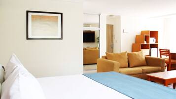 Una habitación de hotel con una cama, un sofá, una mesa de centro y un televisor al fondo.