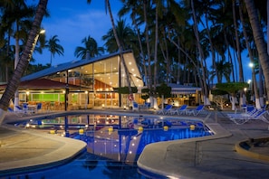 Un hotel moderno con piscina, palmeras y un área de bar o sala de estar.