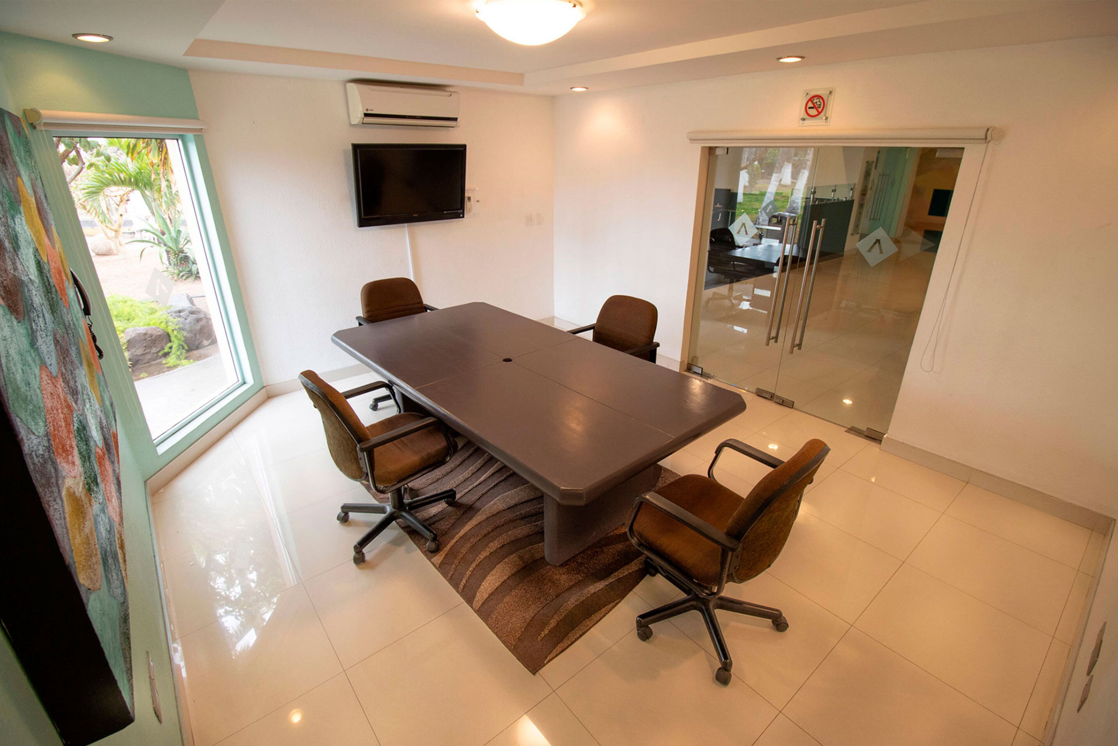 A conference room with a large table, six chairs, a flat-screen TV, and a glass door leading outside.