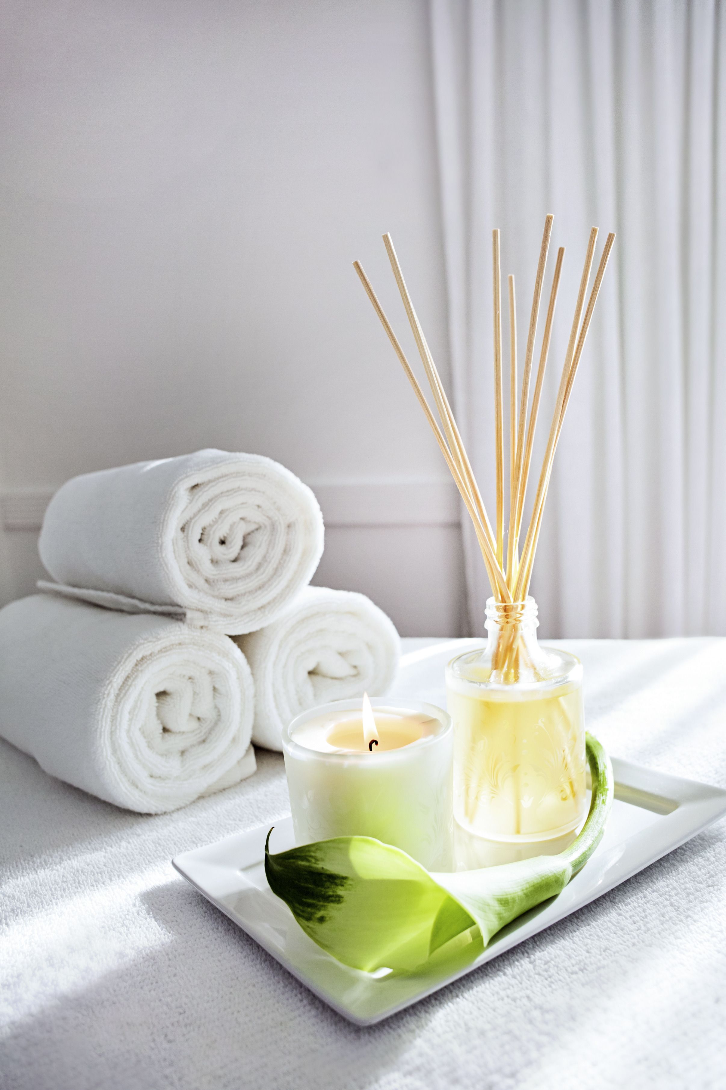A tray with rolled white towels, a candle, reed diffuser, and a green leaf.