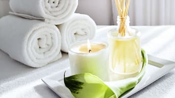 Un vassoio con asciugamani arrotolati bianchi, una candela, diffusore di rattan e una foglia verde.