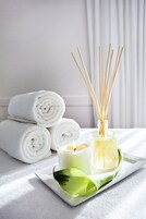 Un vassoio con asciugamani arrotolati bianchi, una candela, diffusore di rattan e una foglia verde.