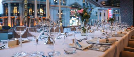 A long dining table set with multiple wine glasses, candles, and cutlery, with a view of a historic building in the background.