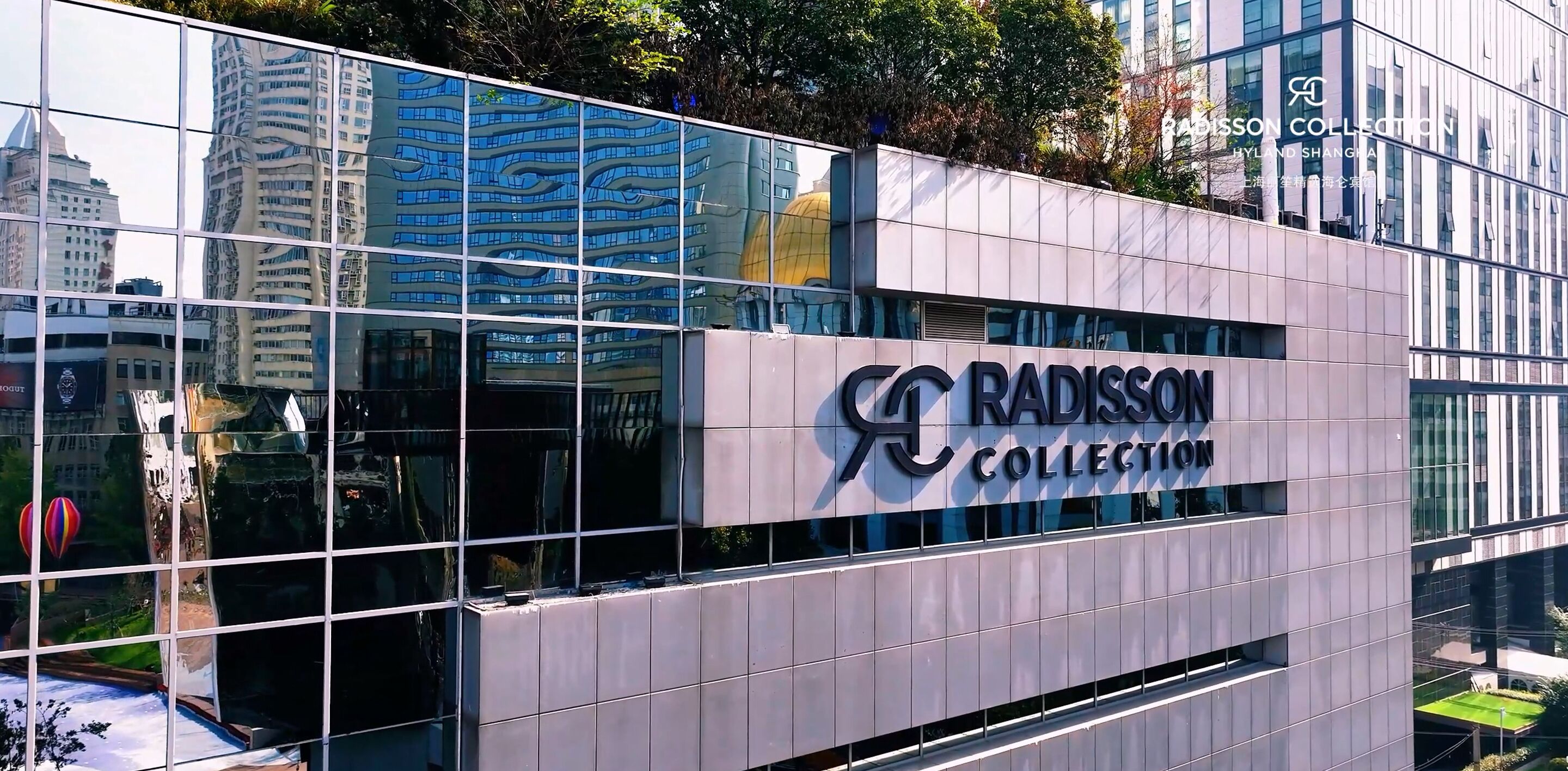 A modern building with a glass facade reflecting surrounding skyscrapers. The building has a sign that reads "RADISSON COLLECTION."