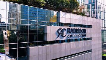 A modern building with a glass facade reflecting surrounding skyscrapers. The building has a sign that reads "RADISSON COLLECTION."