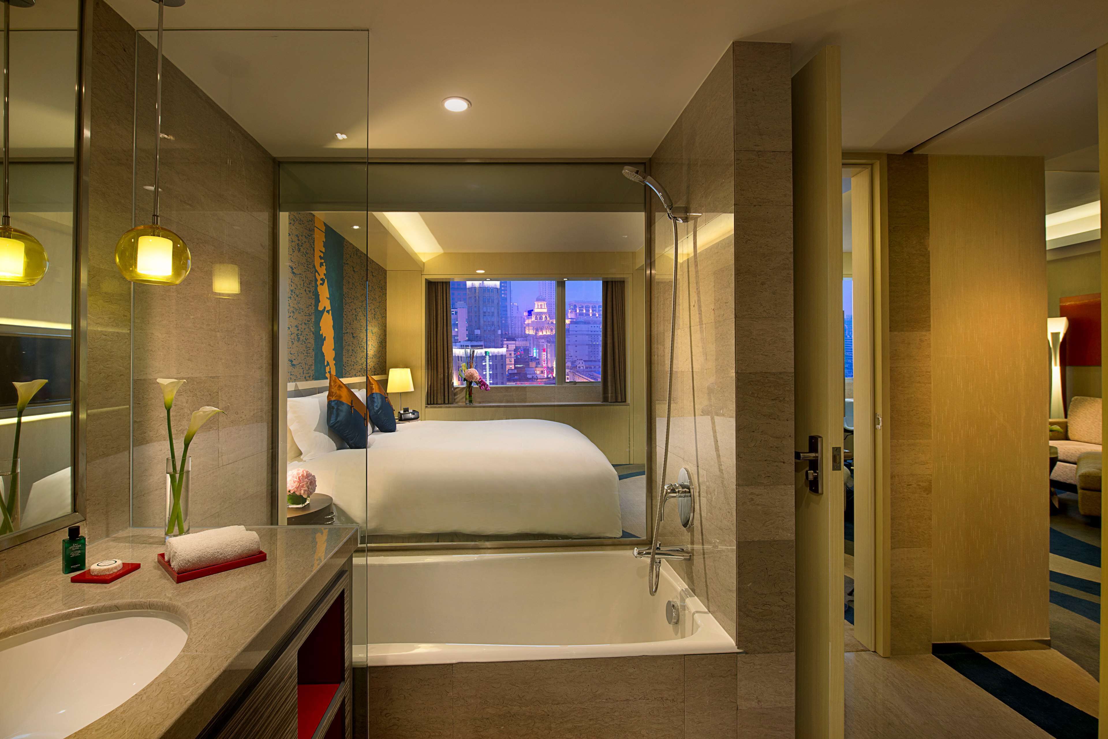 A modern hotel room with a large bed, a separate bathtub, a vanity with a mirror, and a view of the cityscape.
