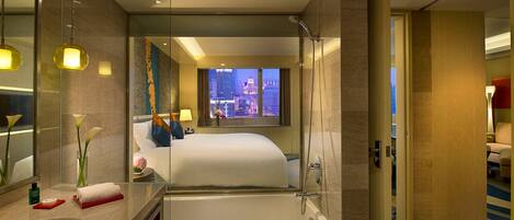 A modern hotel room with a large bed, a separate bathtub, a vanity with a mirror, and a view of the cityscape.