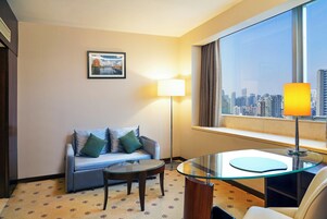 A hotel room with a sofa, a glass table, a lamp, and a city view through the window.