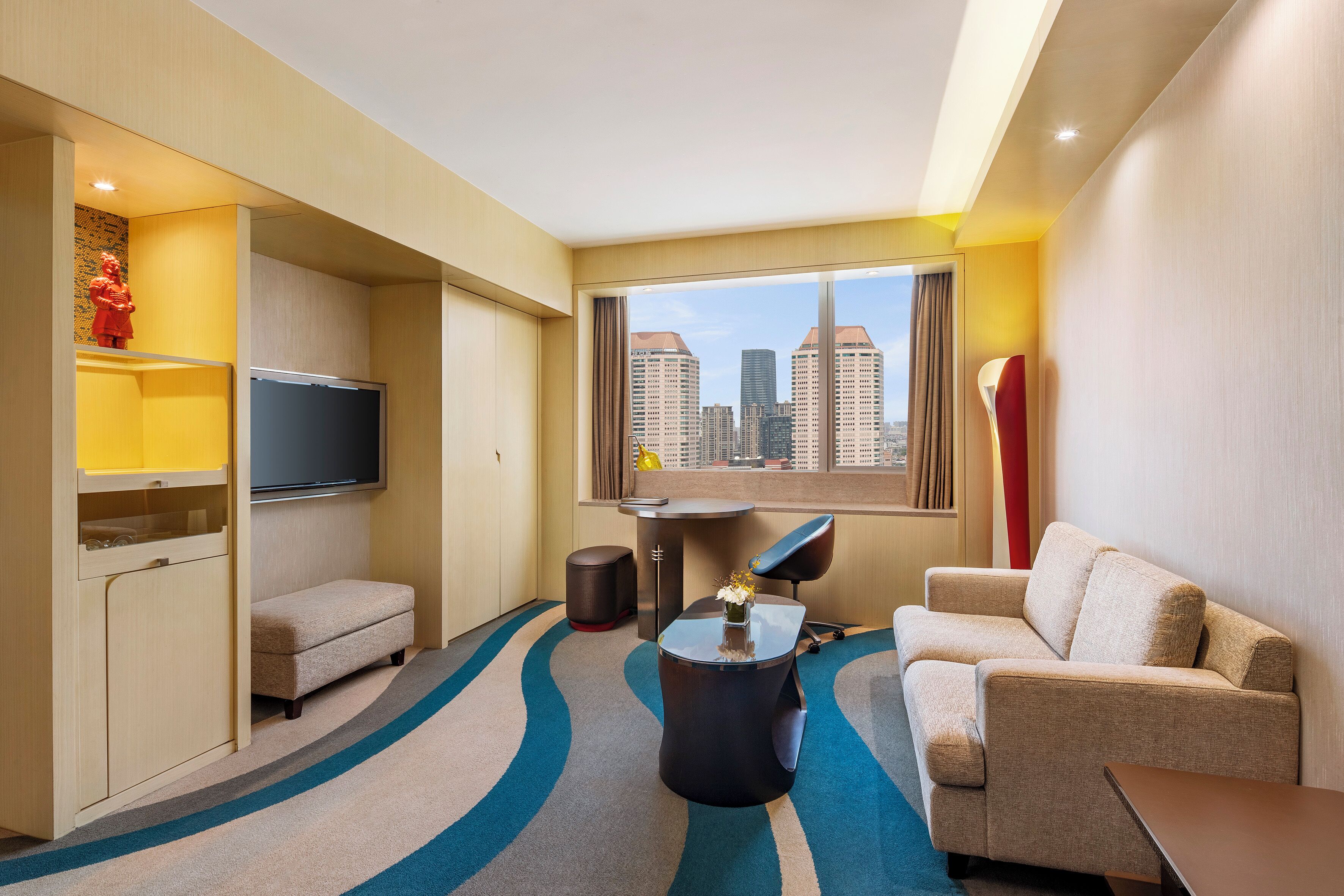 A hotel room with a sofa, armchair, TV, and a city view.
