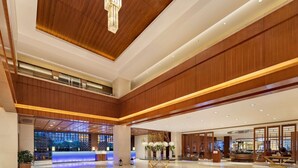 A spacious lobby with a reception desk, wooden paneling, and a modern chandelier.