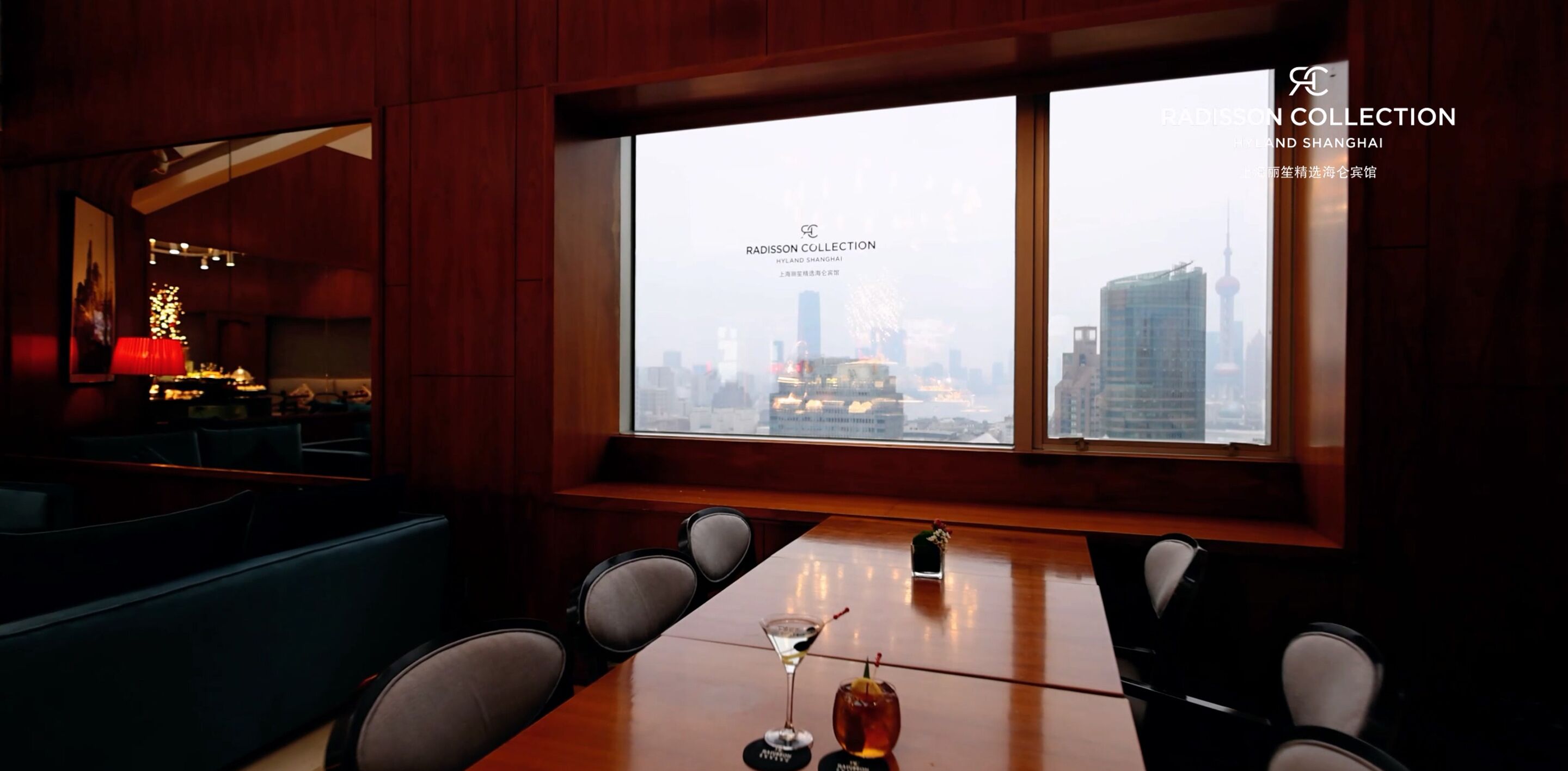 A conference room with a city view, a table with a glass of wine, and a red lamp.