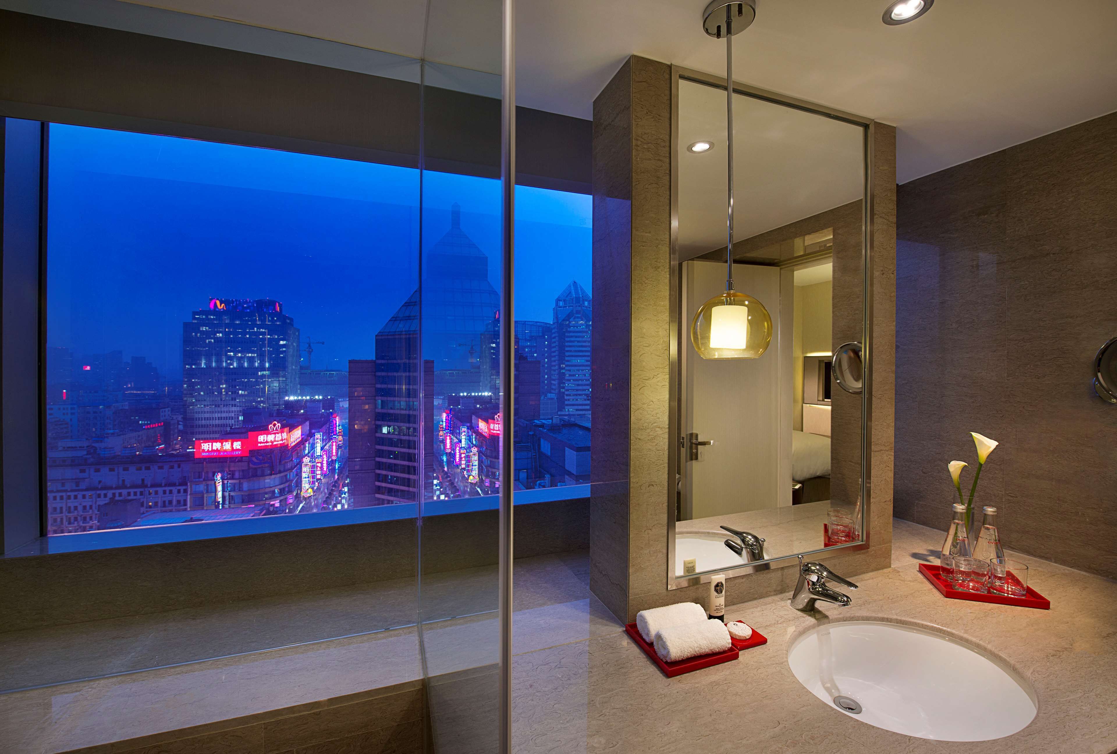 Un baño moderno con un espejo grande, un lavamanos y un ventanal con vistas a la ciudad.