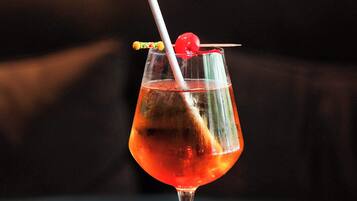 A cocktail in a stemmed glass with a cherry garnish and a straw, placed on a dark surface.