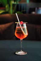 A cocktail in a stemmed glass with a cherry garnish and a straw, placed on a dark surface.